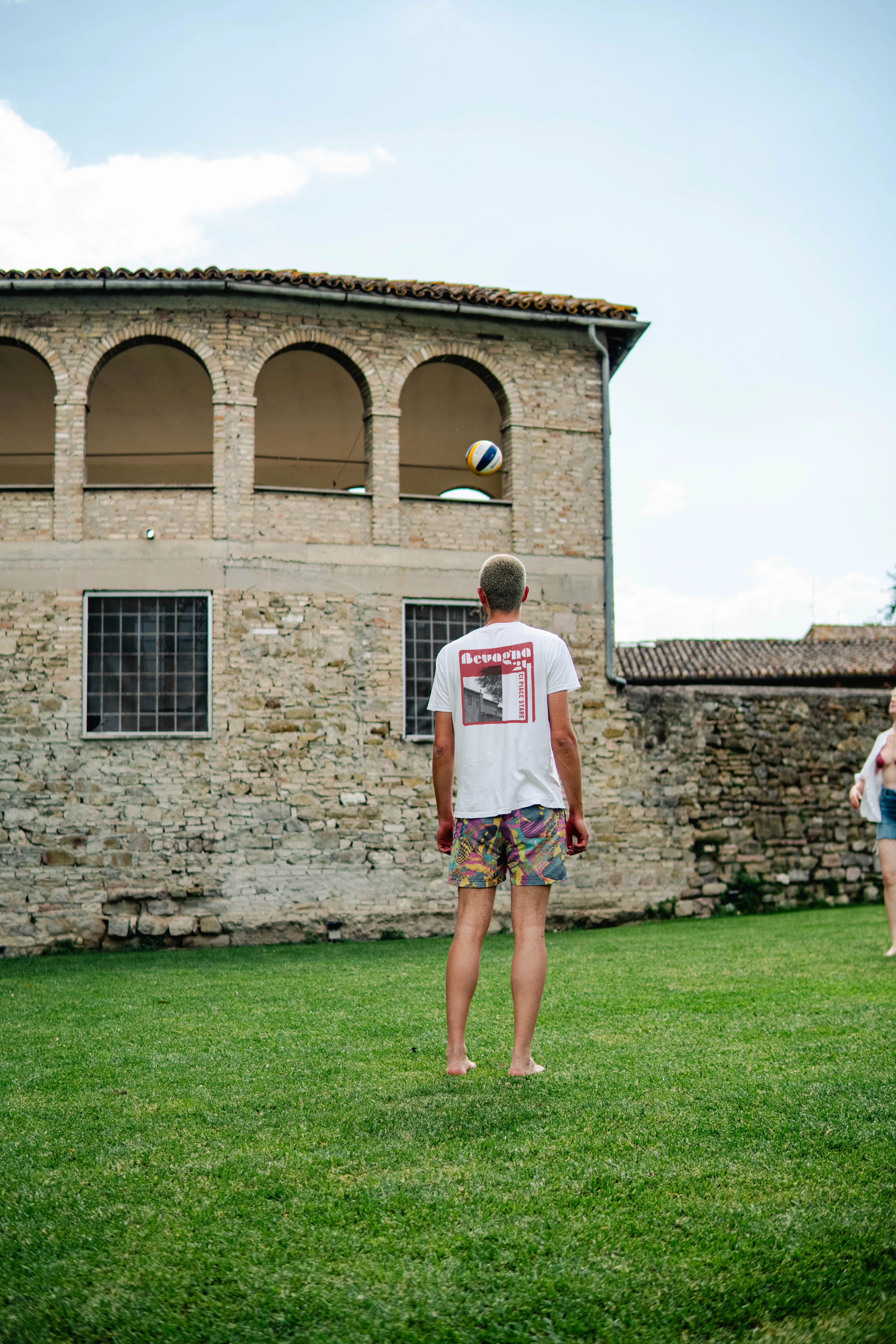 Raphael trägt bedrucktes T-Shirt auf einer Wiese vor historischer Architektur in Bevagna