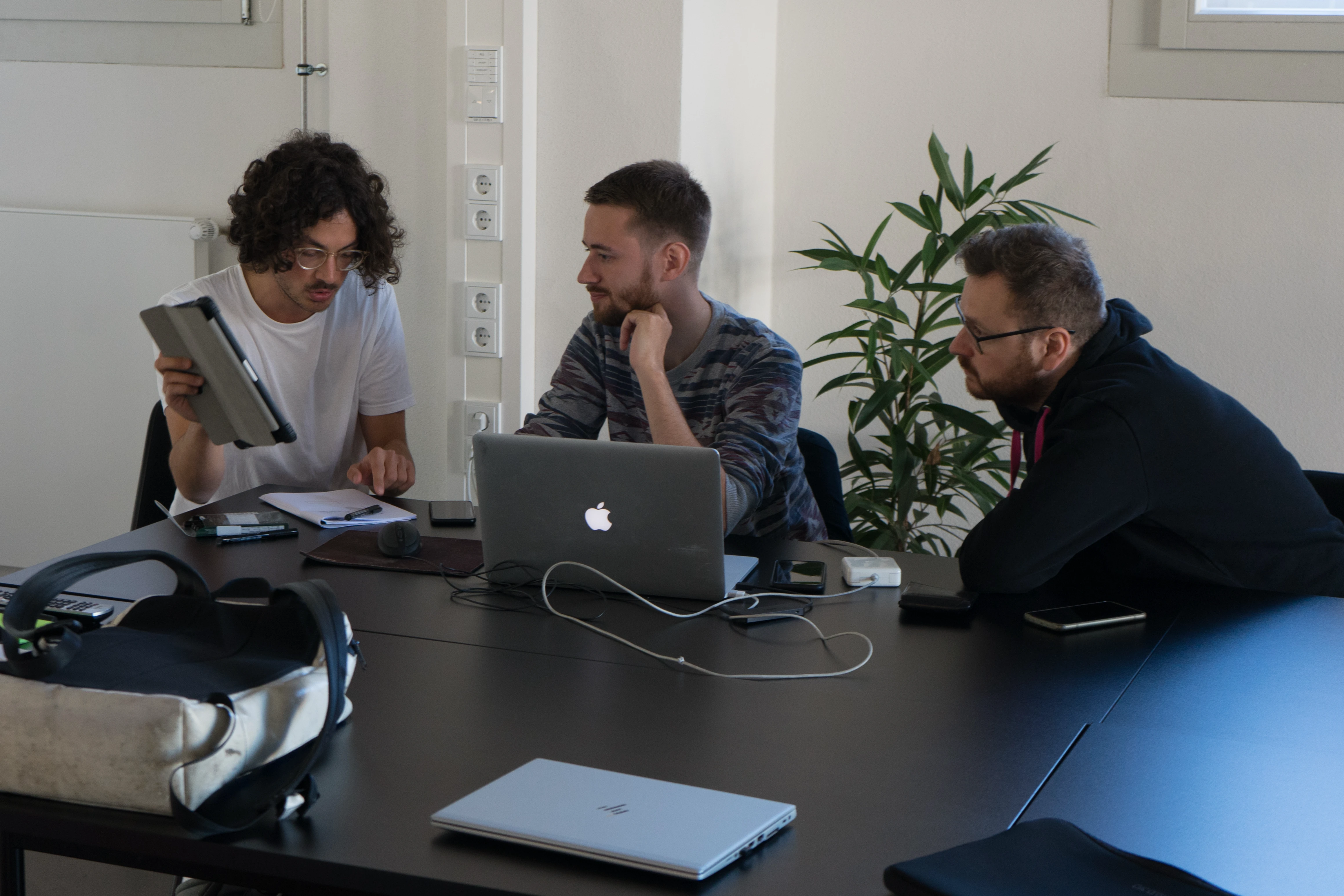 Raphael und zwei weitere Entwickler arbeiten gemeinsam an Konzept und Interface mit Laptop und Tablet